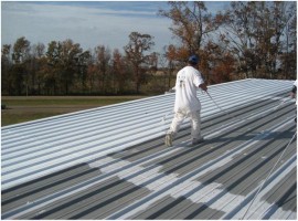 Applicator rolling protective restoration coating across a standing seam metal roof